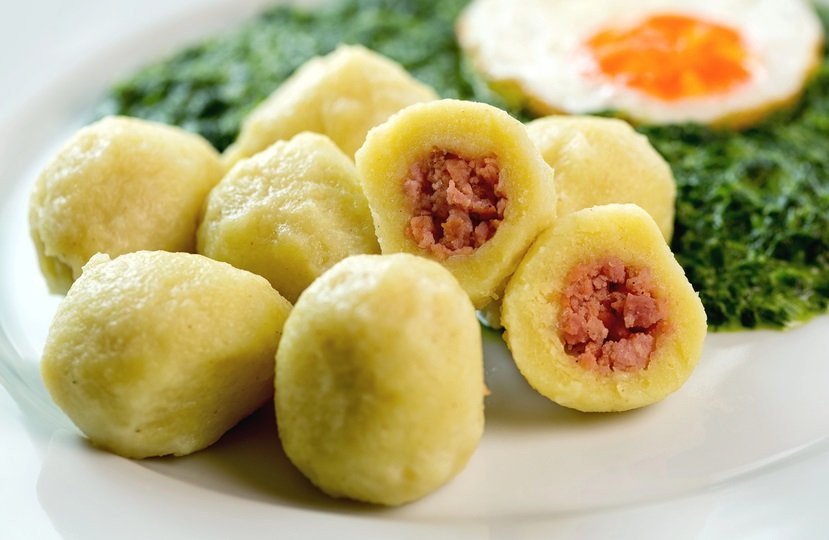 Fleischknödel mit Erdäpfelteig mit Spinat und Spiegelei auf einem Teller.