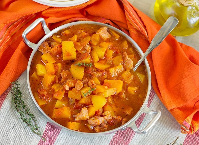 Buntes Kürbisragout mit Kartoffeln in einem Kochtopf serrviert.